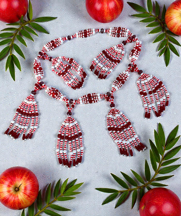 Red and white beaded necklace on a light gray background with red apples and green leaves.
