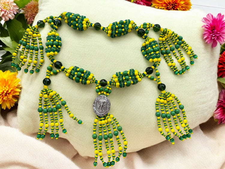 A beaded necklace with green and yellow strings arranged in a pattern, featuring a medallion with an elephant design.