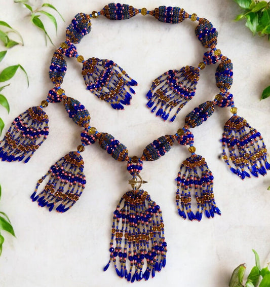 A vibrant beaded mazo featuring sapphire blue, topaz, and pink coral with a bow and arrow accent, displayed against a white background with green leaves.