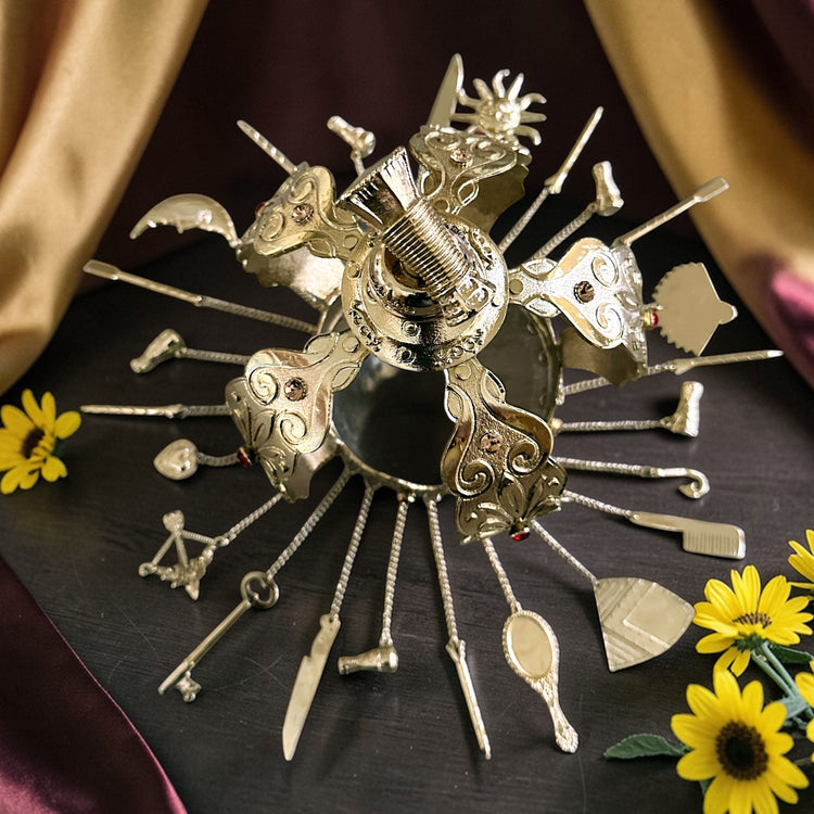 Decorative metal gold colored crown with various small objects on a dark surface with yellow flowers.