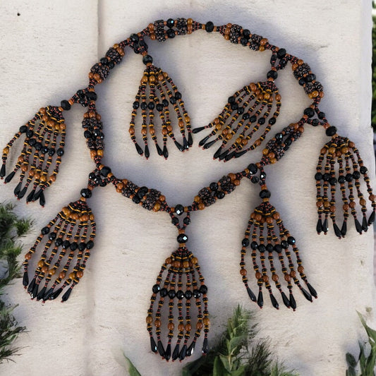 A traditional Yoruba-style beaded necklace with a 4-string mazo design, featuring black and brown beads, displayed against a white background with green accents.