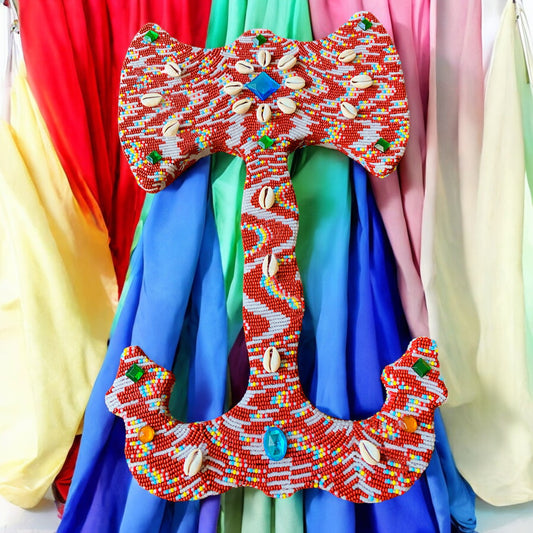 Colorful beaded double headed axe with shells and stones against a multicolored fabric background