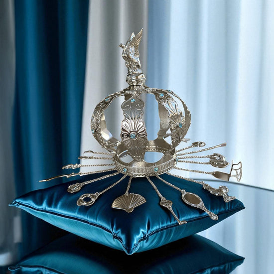 Decorative silver crown on a blue pillow with a blurred curtain background