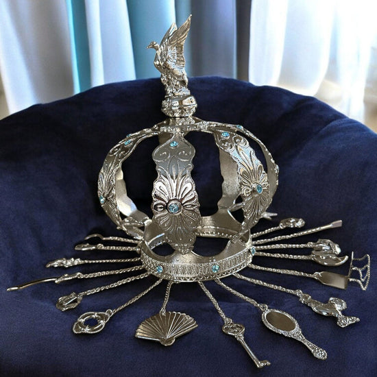 Decorative silver crown with intricate designs on a dark blue cushion.