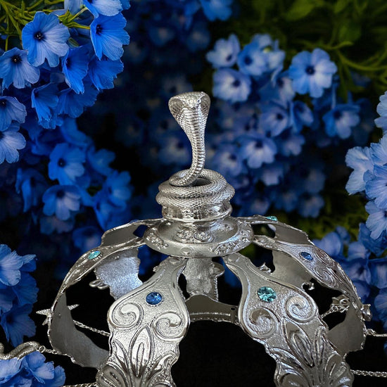 Decorative silver crown with snake design against a background of blue flowers