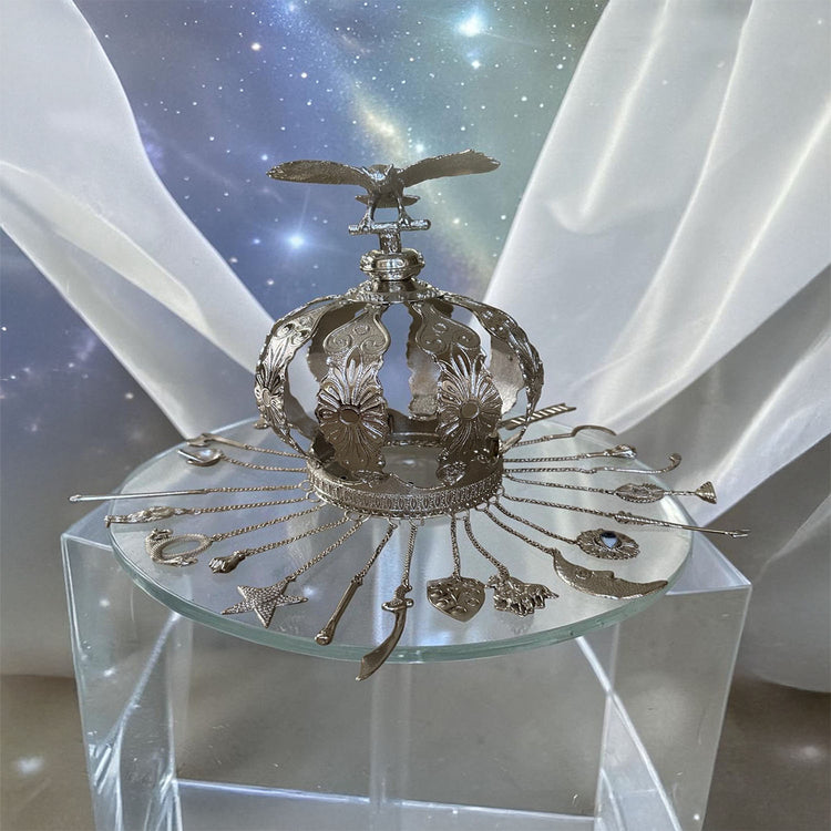 Decorative silver colored crown on a clear pedestal with a starry background and sheer white curtains