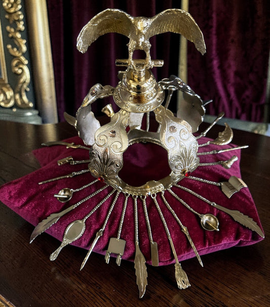 Decorative gold colored crown with red and amber colored stones on a burgandy cushion