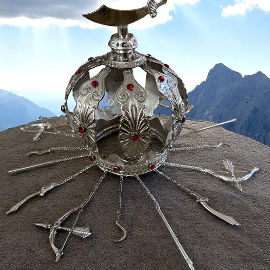 Decorative silver metal crown with red gemstones and a sabre topper on a mountainous background