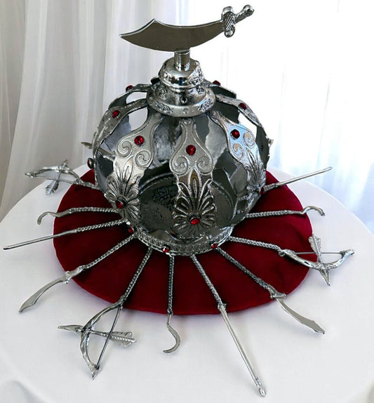 Decorative silver metal crown with red gemstones and a sabre topper on a white background