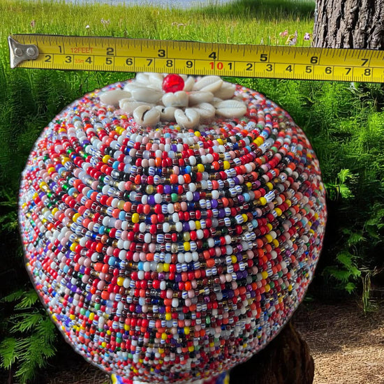 Multicolored beaded gourd with a measuring tape against a natural background.