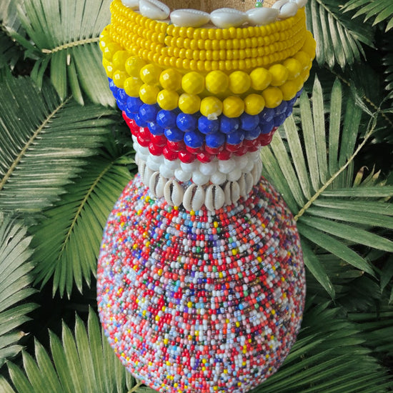 Colorful beaded gourd with cowrie shells on green leaves