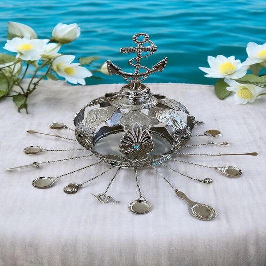 A nickel-plated crown with aqua marine blue rhinestones and various symbolic tools placed around it, displayed on a table with a serene background.