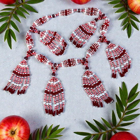 Red and white beaded necklace on a light gray background with red apples and green leaves.