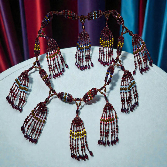 Beaded necklace with multiple strands and pendants on a white surface with a colorful curtain background.