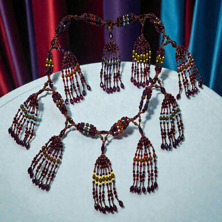 Beaded necklace with multiple strands and pendants on a white surface with a colorful curtain background.