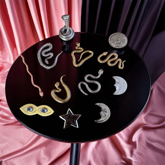 Nana Buruku tool set items including snakes, stars, and moons on a round black surface with pink fabric background.