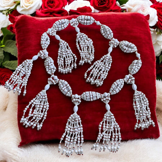 A white acrylic beaded necklace with red accents, displayed on a red cushion with a floral background.
