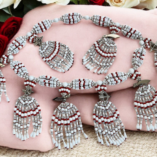 A detailed image of a Yoruba-style mazo, featuring a 10-string design with white, red, and silver beads, ornate with metal clasps and ceremonial embellishments.