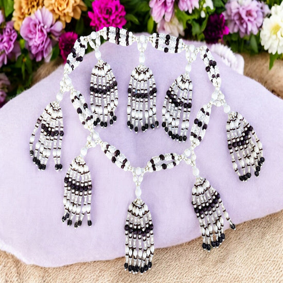A petite necklace with white and purple beads, designed for the Obatala path, displayed on a fabric surface with a floral pattern in the background.