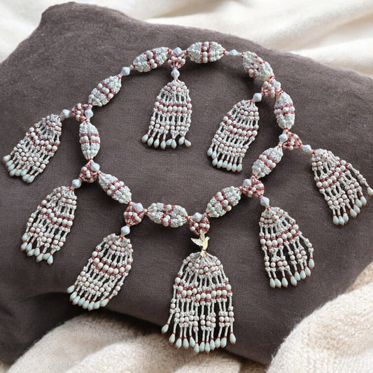 A detailed image of a 10-string mazo necklace with white and coral beads, featuring a decorative dove accent, displayed on a dark cushion.