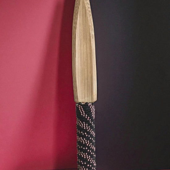 Decorative bamboo knife with a beaded handle on a pink and black background