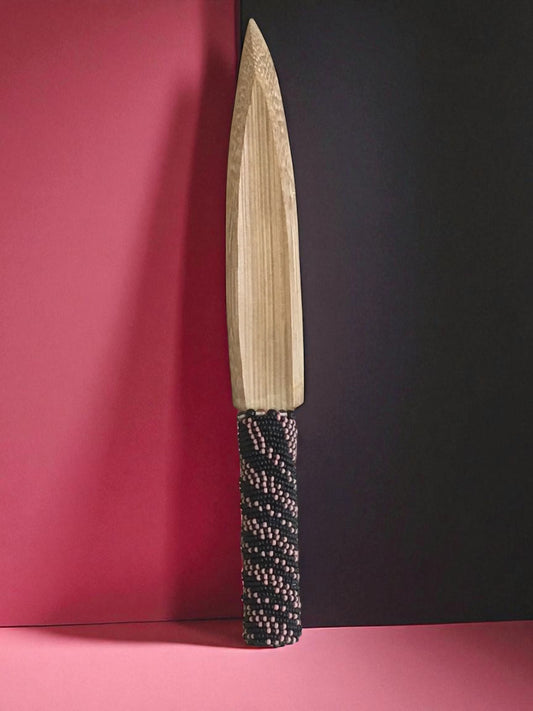 Decorative bamboo knife with a beaded handle on a pink and black background
