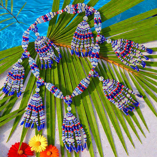 Beaded necklace with blue, red, and white pattern on a palm leaf with flowers.
