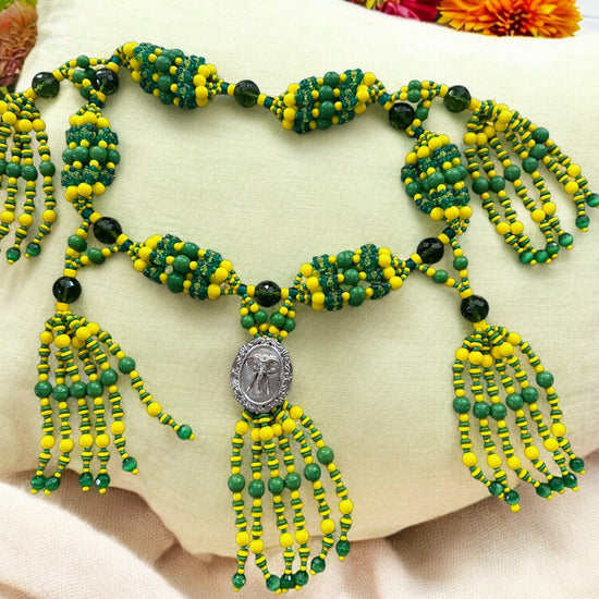 A beaded necklace with green and yellow strings arranged in a pattern, featuring a medallion with an elephant design.