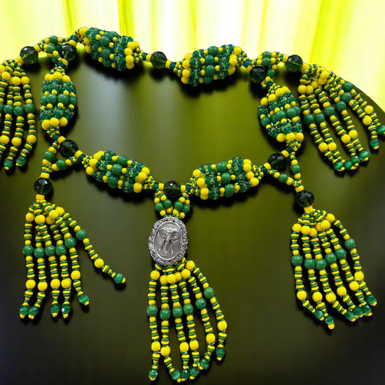 Green and yellow beaded necklace with elephant medallion on a dark surface.