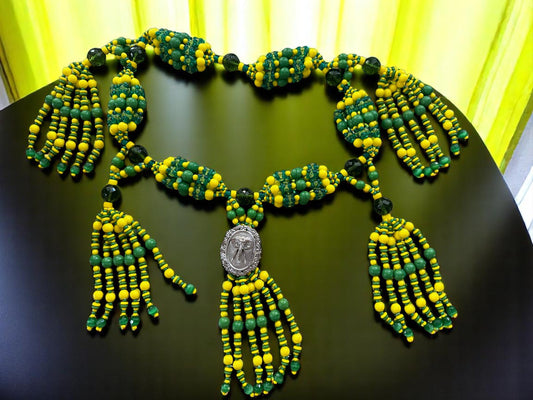Green and yellow beaded necklace with elephant medallion on a dark surface.