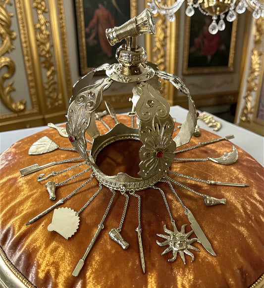 Decorative gold metal crown with adornments on a amber velvet pillow with ornate background.