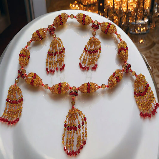 A radiant 10-string acrylic mazo (necklace) with topaz, red, and pink coral beads, featuring Ikolé path attributes, displayed on a white surface with a reflective background.