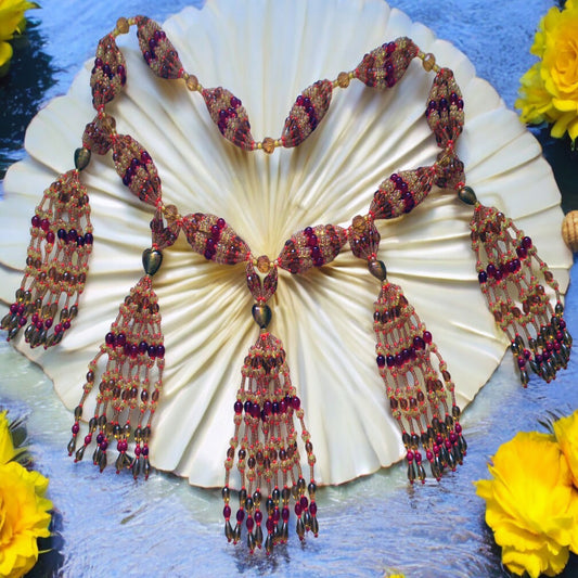 A detailed image of a 10-string mazo (necklace) for Oshun (Ikole) made with topaz and red Czech glass beads, displayed on a white circular base with yellow flowers around it.
