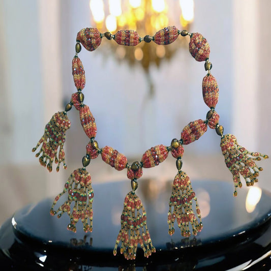 A detailed image of a 10-string mazo for Oshun Ololodi, featuring intricate designs with topaz, green, and pink coral colored beads, and ornate tassels.