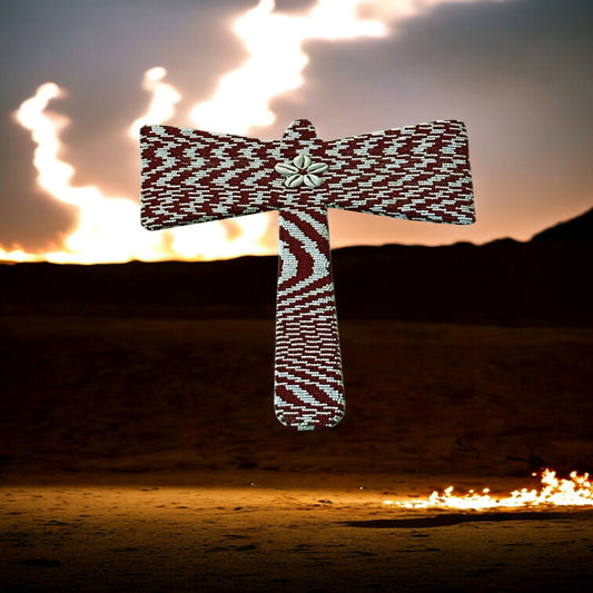 A double-edged, beaded axe with red and white beads and cowrie shells, displayed against a backdrop with flames.
