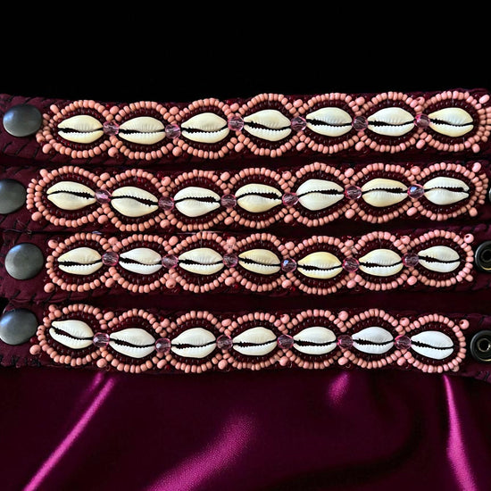 Stack of beaded cowrie bracelets on a burgandy background